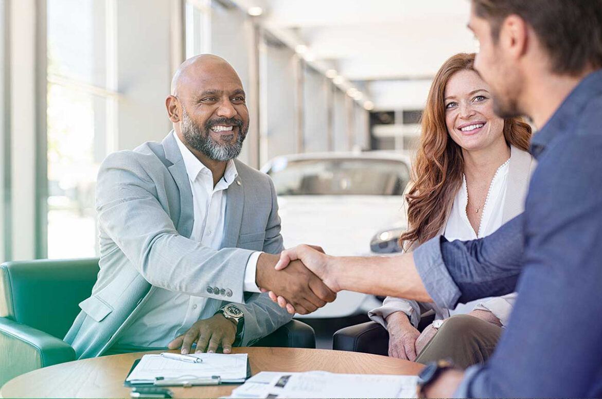 A male auto dealerships owner shaking hands with a new customer