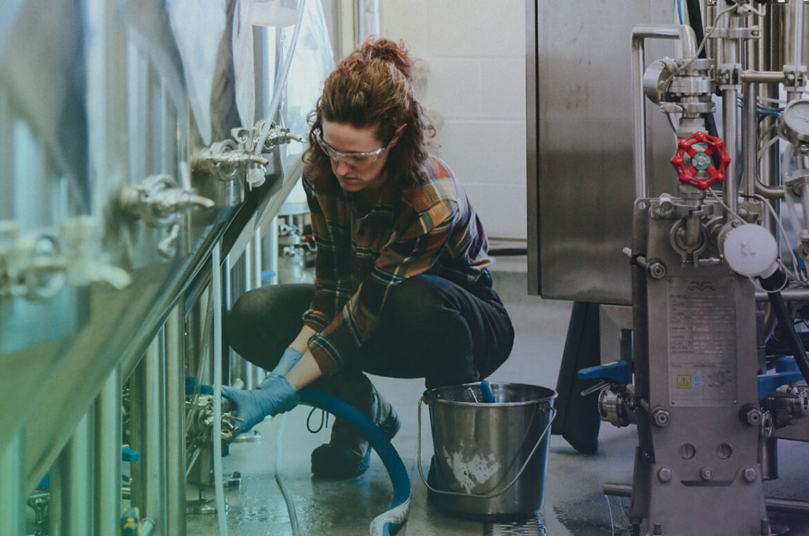A female craft brewery employee about to empty a brewing tank