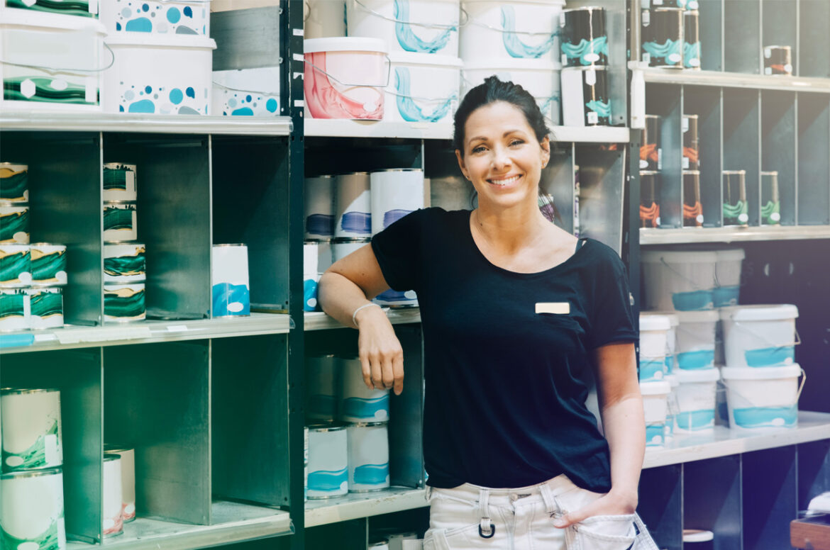 A female hardware store business owner is standing in her store near shelves of products.